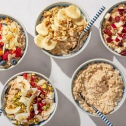 An overhead photo of 5 bowls of oatmeal with spoons. Four have various toppings and one is plain.
