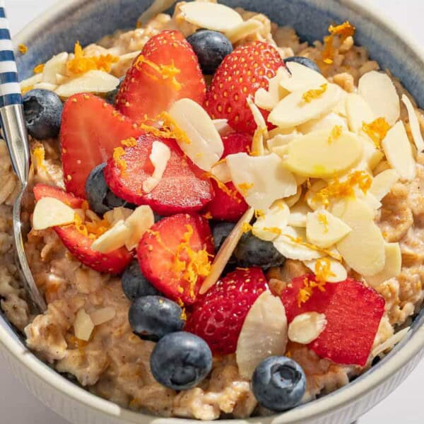 Oatmeal topped with strawberries, blueberries, chia seeds, almonds and orange zest in a bowl with a spoon.