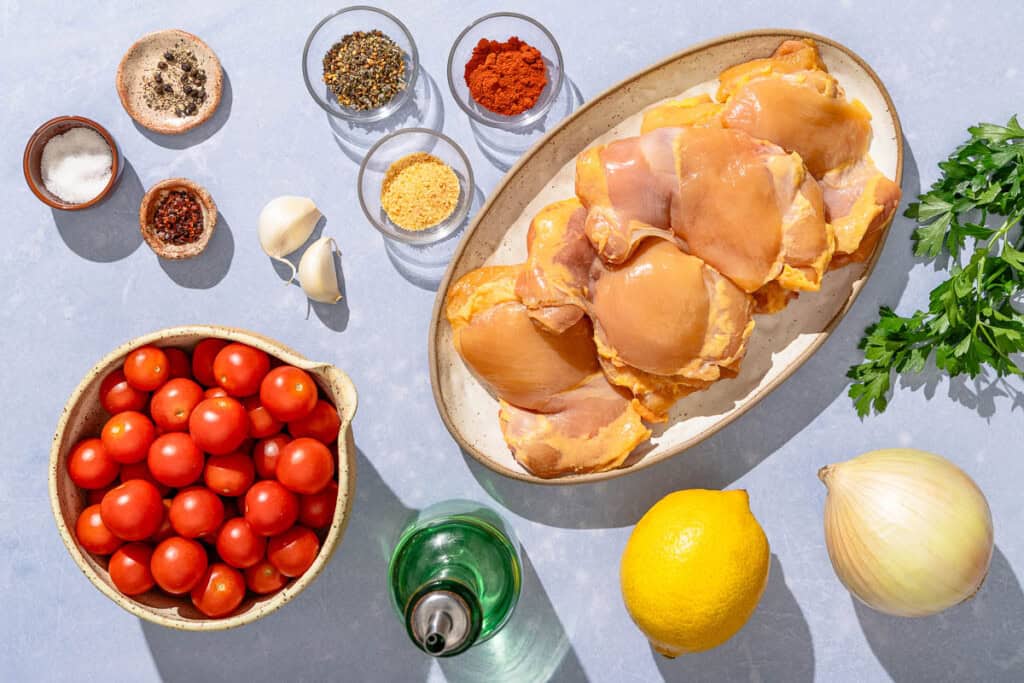 Ingredients for skillet chicken thighs including chicken thighs, cherry tomatoes, za'atar, sweet spanish paprika, garlic powder, aleppo pepper, salt, black pepper, olive oil, onion, garlic, lemon and parsley.