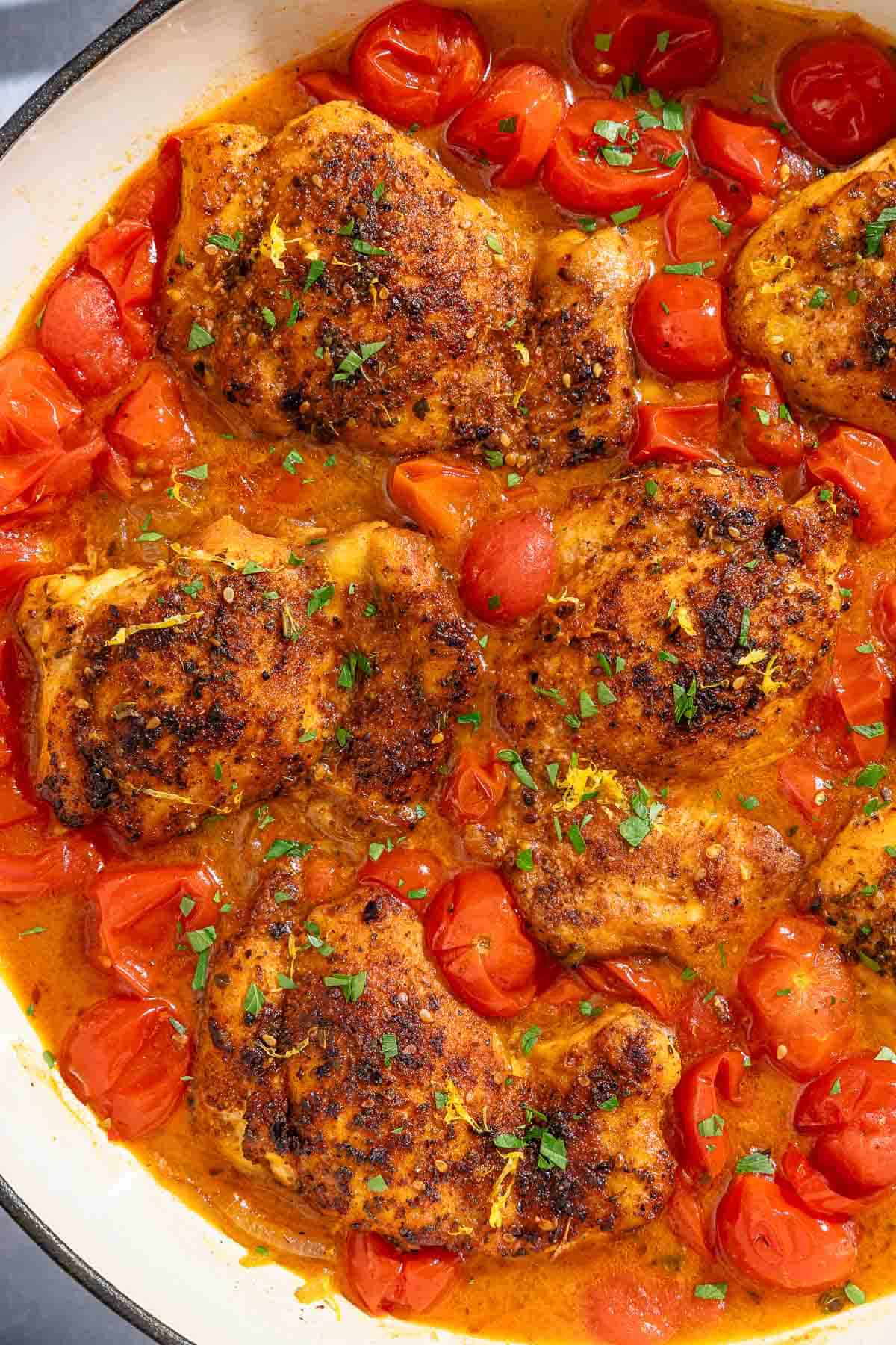 Chicken thighs in a cherry tomato sauce in a skillet.