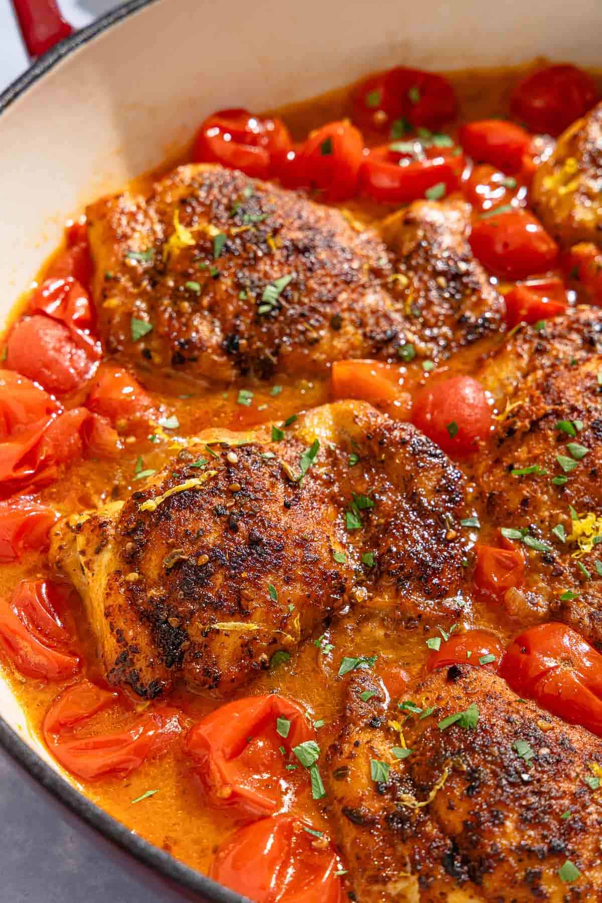 A closeup of chicken thighs in a cherry tomato sauce in a skillet.