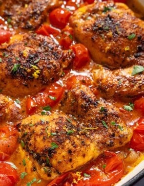A closeup of chicken thighs in a cherry tomato sauce in a skillet.