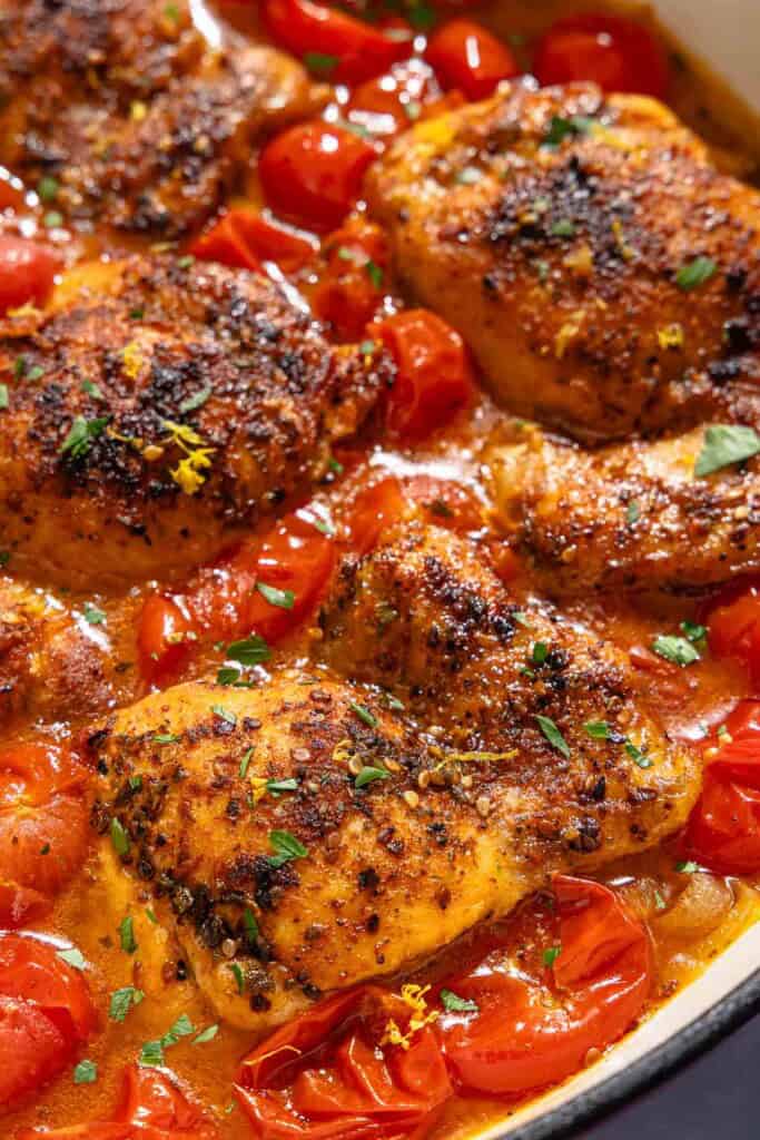 A closeup of chicken thighs in a cherry tomato sauce in a skillet.