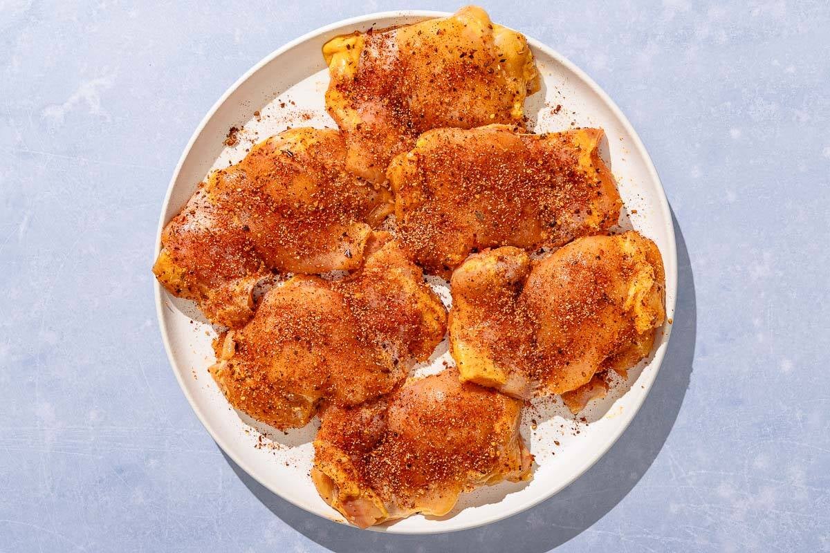 Seasoned, uncooked chicken thighs on a plate.