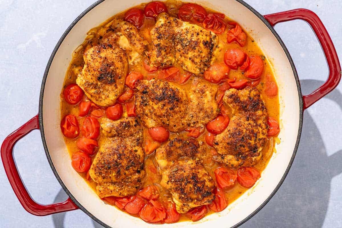 Chicken thighs in a cherry tomato sauce in a skillet.