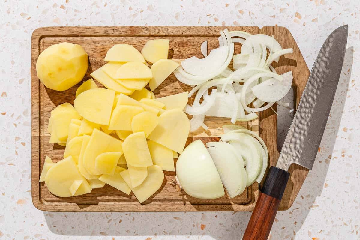 The sliced potatoes and onions for the spanish tortilla on a cutting board with a knife.