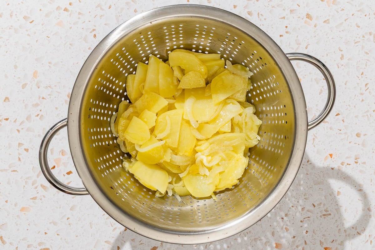 The cooked sliced onions and potatoes for the spanish tortilla draining in a colander.