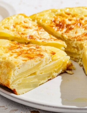 A close up of the partially sliced spanish tortilla on a platter with one sliced removed.