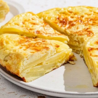 A close up of the partially sliced spanish tortilla on a platter with one sliced removed.