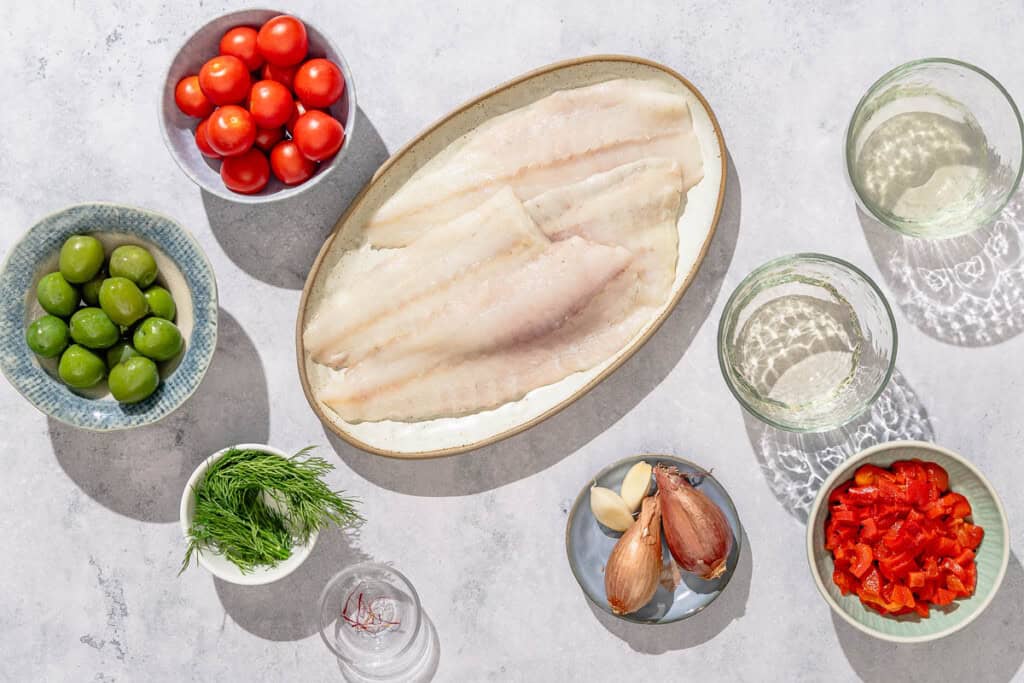 Ingredients for stuffed flounder including flounder fillets, olive oil, shallots, grape tomatoes, roasted red peppers, castelvetrano olives, fresh dill, salt, black pepper, chicken stock, white wine, garlic, and saffron.