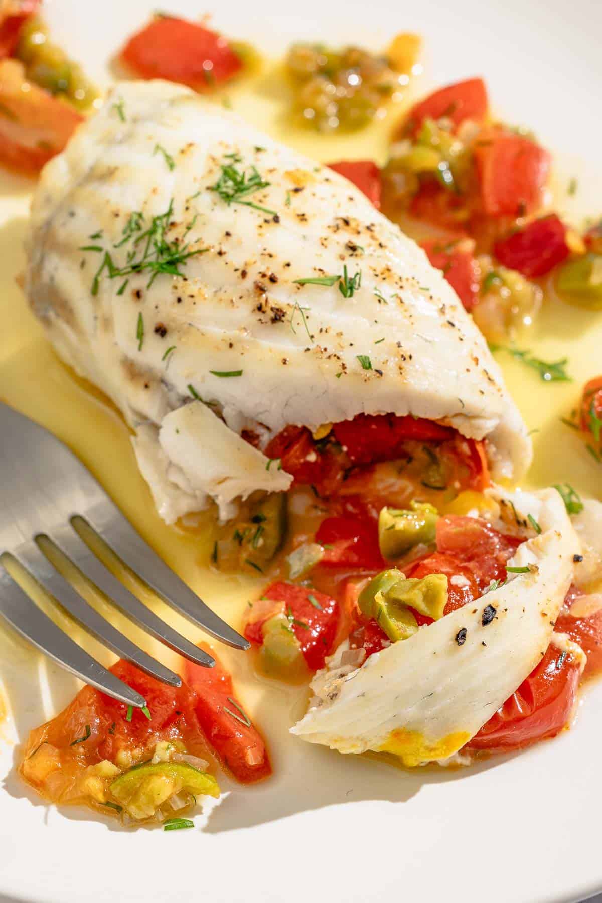 A close up of a stuffed flounder fillet on a plate with a fork.