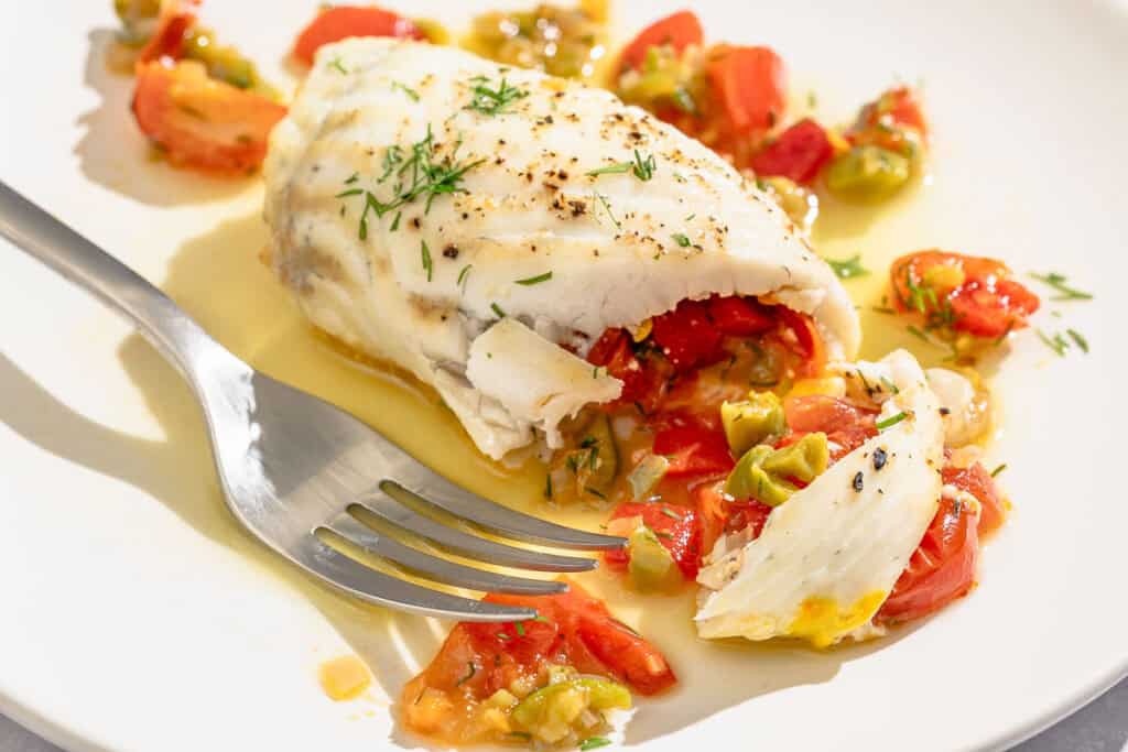 A close up of a stuffed flounder fillet on a plate with a fork.