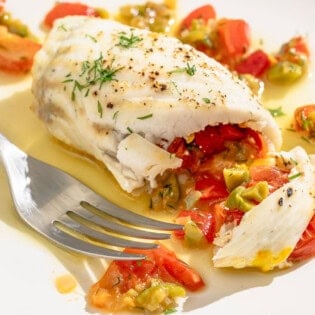 A close up of a stuffed flounder fillet on a plate with a fork.
