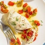 A stuffed flounder fillet on a plate with a fork and a slice of crusty bread.