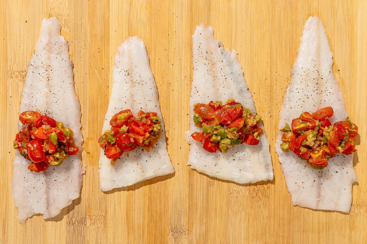 Four flounder fillets topped with stuffing on a cutting board just before being rolled.