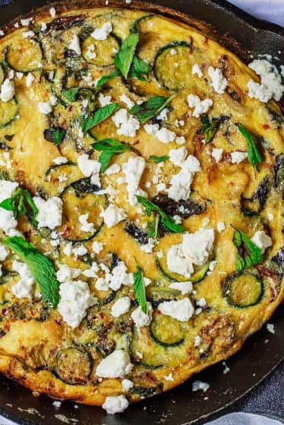 Overhead shot of a Middle Eastern zucchini baked omelet in a pan garnished with feta and mint. 