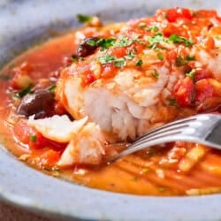 A close up of a serving of provençal fish in a bowl with a fork.