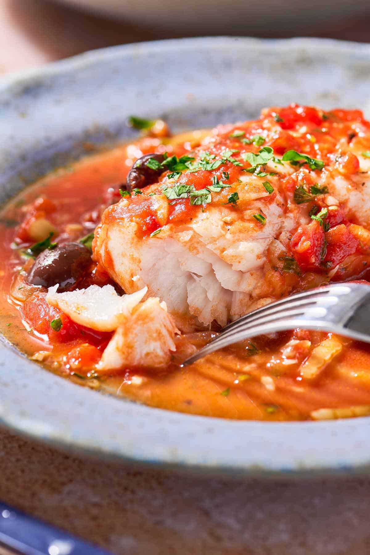 A close up of a serving of provençal fish in a bowl with a fork.