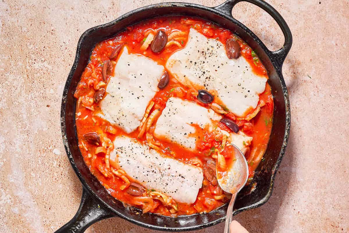 The sauce for the provençal fish being spooned over the nestled pieces of haddock in the case iron skillet.