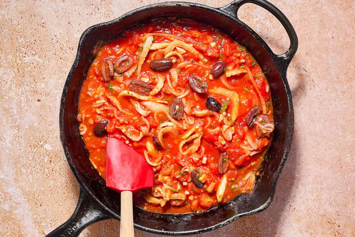 The sauce for the provençal fish in a cast iron skillet with a spatula.