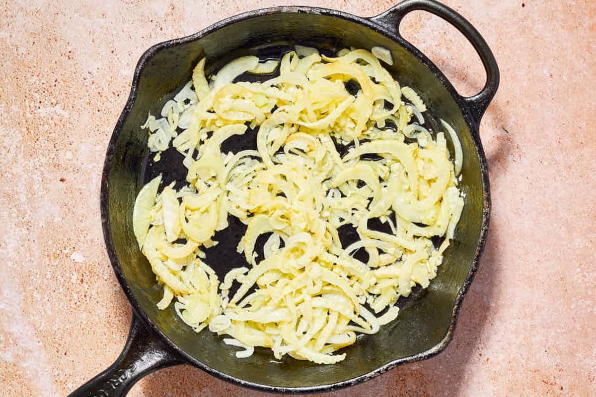 Sliced onions for the provençal fish being sauteed in a cast iron skillet.
