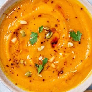 An overhead photo of a bowl of butternut squash apple soup next to a bowl of aleppo pepper.
