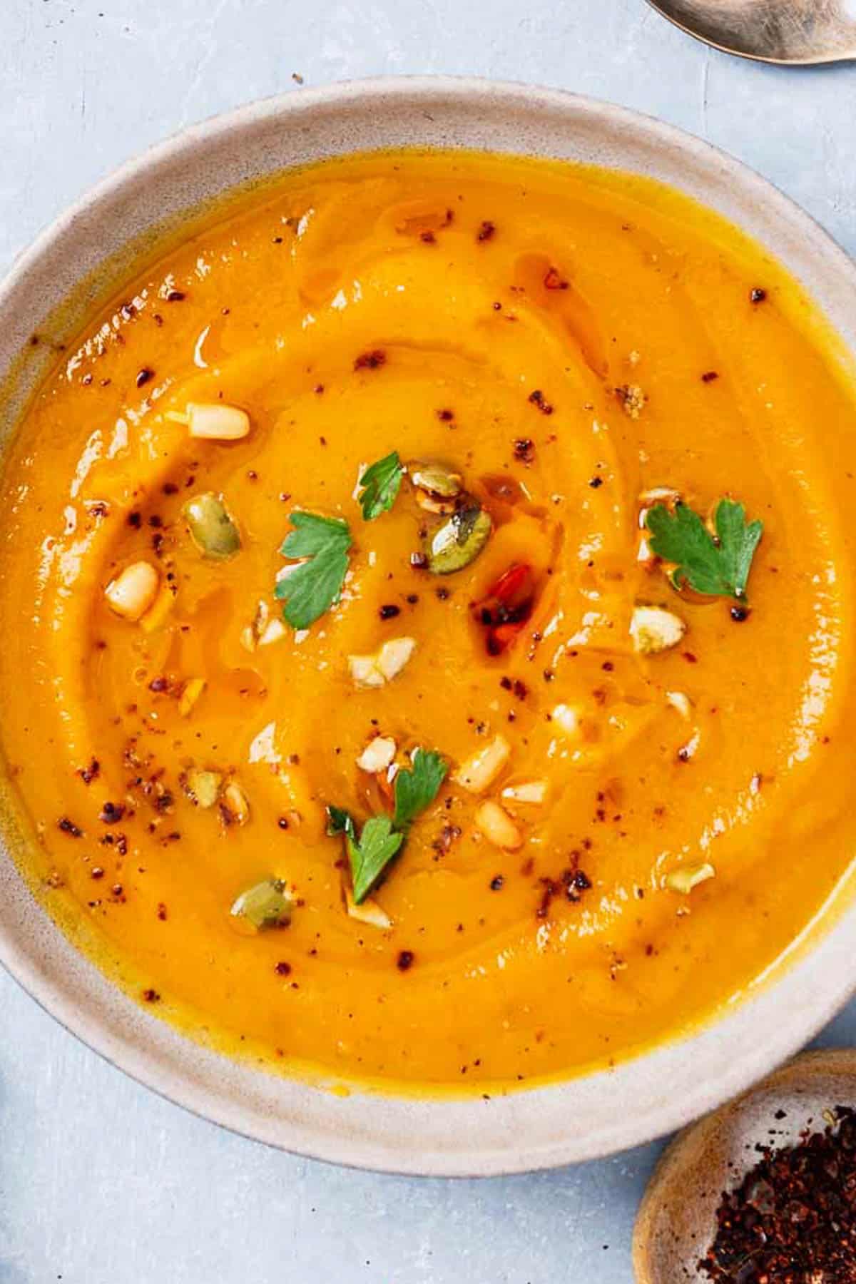 An overhead photo of a bowl of butternut squash apple soup next to a bowl of aleppo pepper.