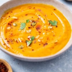 A close up of a bowl of butternut squash apple soup next to an empty bowl and a bowl of aleppo pepper.