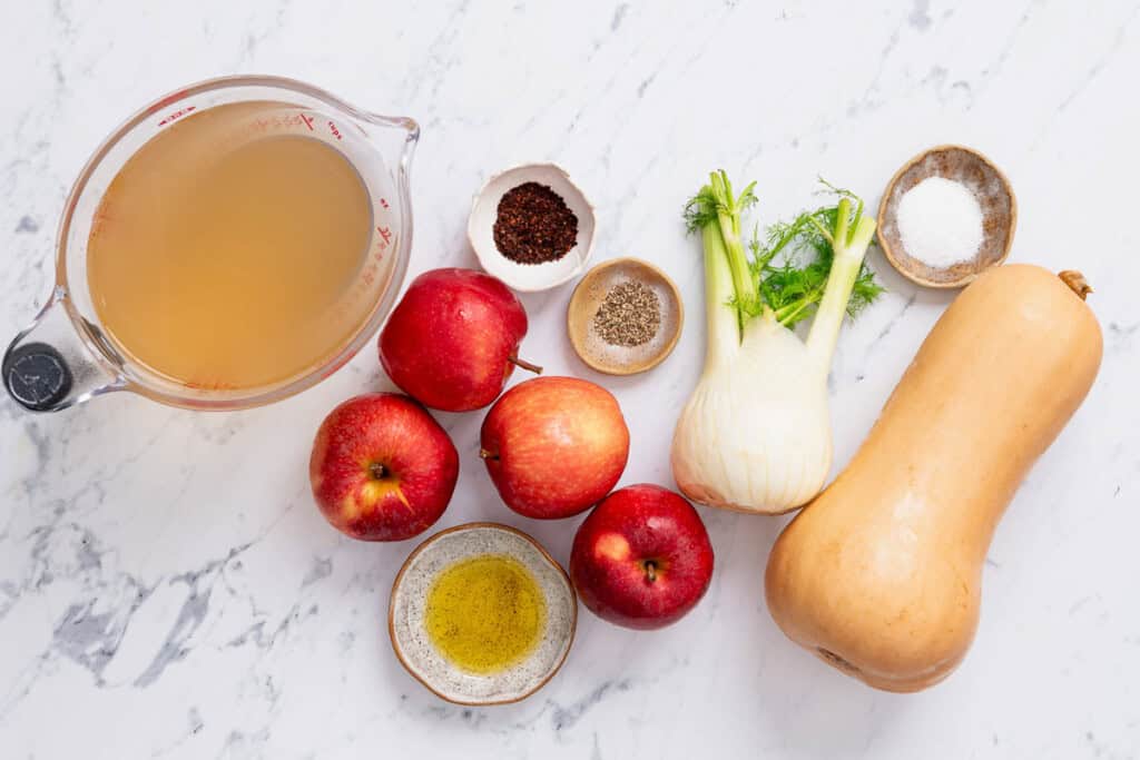 Ingredients for the butternut squash apple soup including vegetable broth, butternut squash, apples, olive oil, salt, fennel, aleppo pepper, apple cider vinegar, and black pepper.