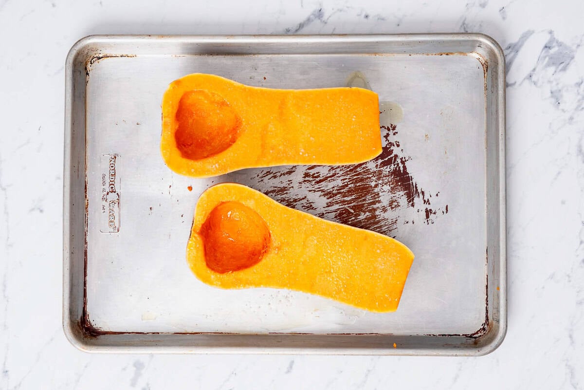 Two uncooked butternut squash halves on a sheet pan.