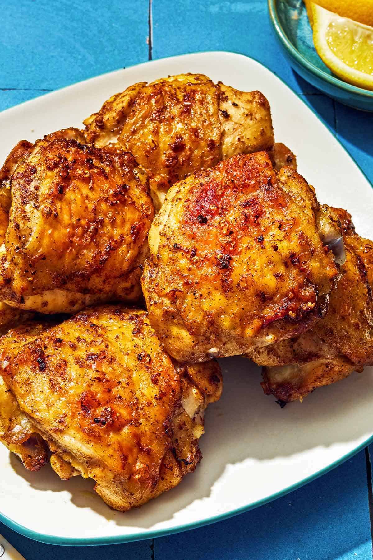 Six air fryer chicken thighs on a plate next to a bowl of lemon wedges.