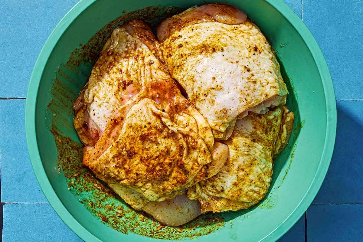 Uncooked chicken thighs in a bowl of marinade.