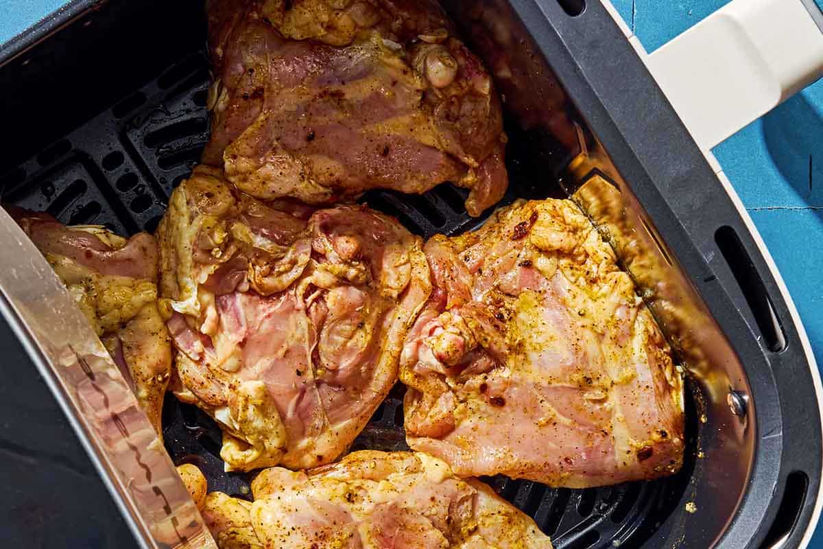 Six uncooked air fryer chicken thighs in an air fryer.