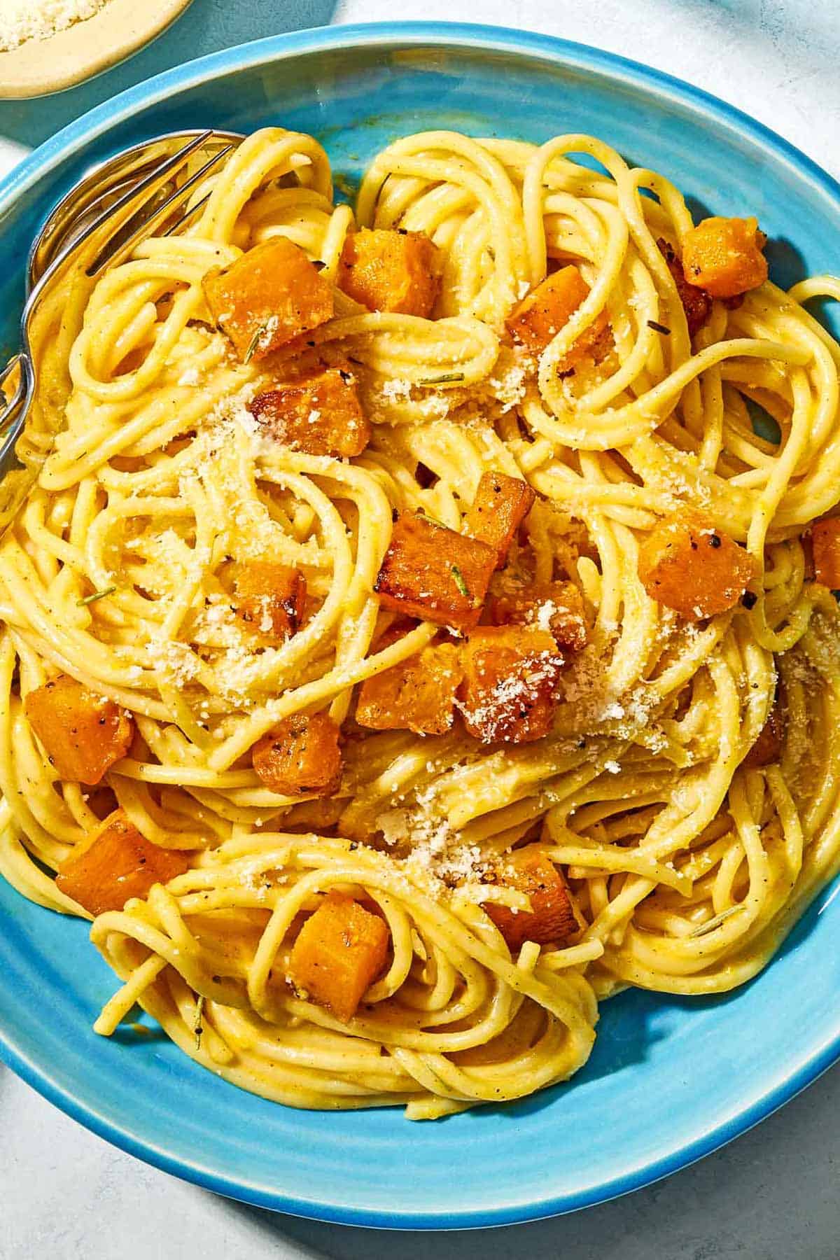A bowl of butternut squash pasta with a fork and spoon.