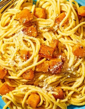 A bowl of butternut squash pasta with a fork and spoon.