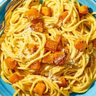 A bowl of butternut squash pasta with a fork and spoon.