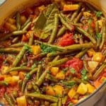 Fasolakia in a large pot next to a small bowl of chopped parsley.