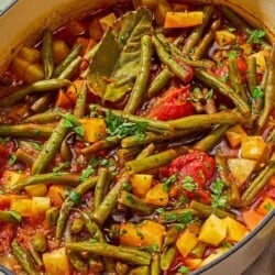 Fasolakia in a large pot next to a small bowl of chopped parsley.