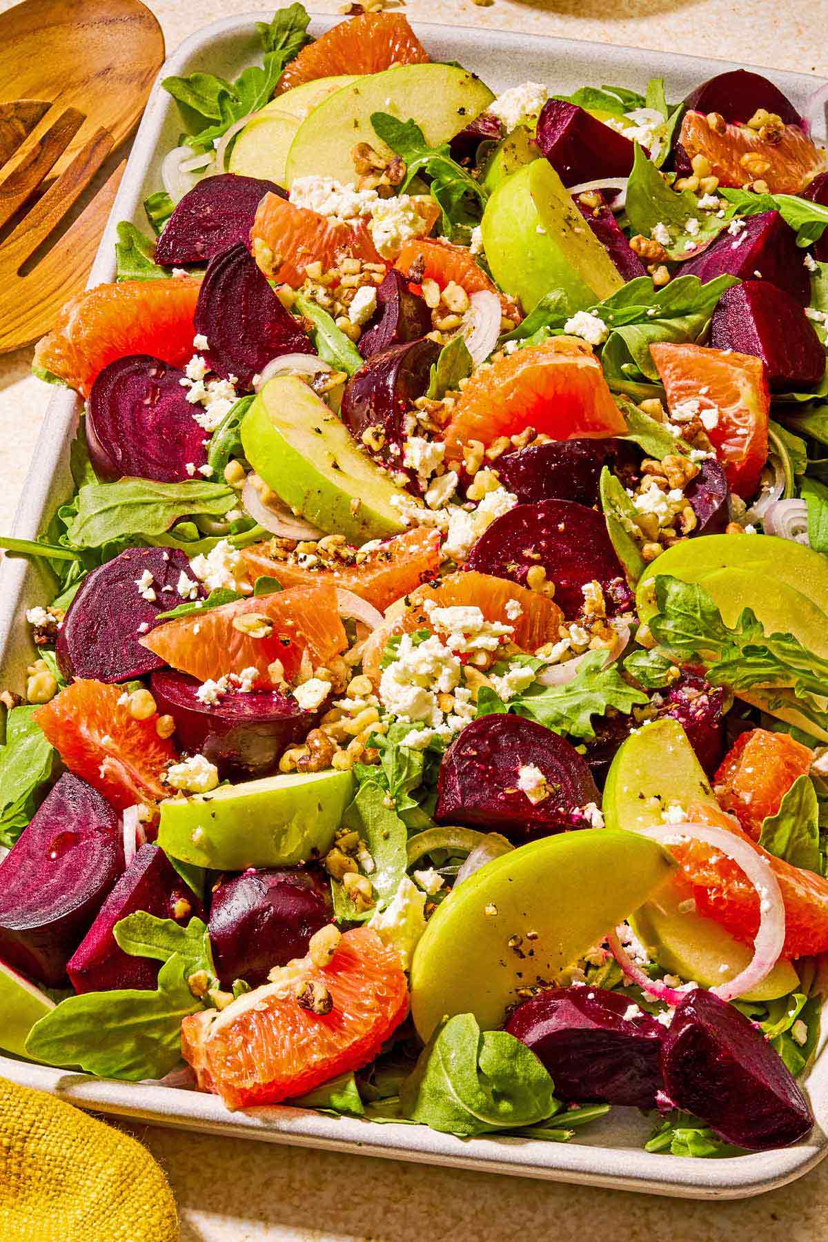 Beet salad on a serving platter next to wooden serving utensils.