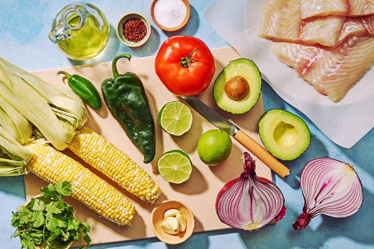 Ingredients for the poached flounder and sweet corn salsa including flounder, ears of corn, cilantro, garlic, red onion, limes, a poblano pepper, a jalapeño pepper, avocado, olive oil, aleppo pepper, and salt.