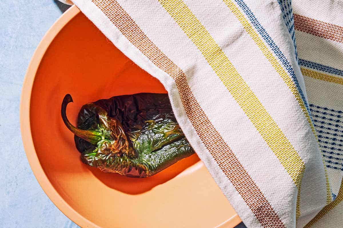 the broiled poblano pepper for the sweet corn salsa in a bowl, partially covered with a kitchen towel.