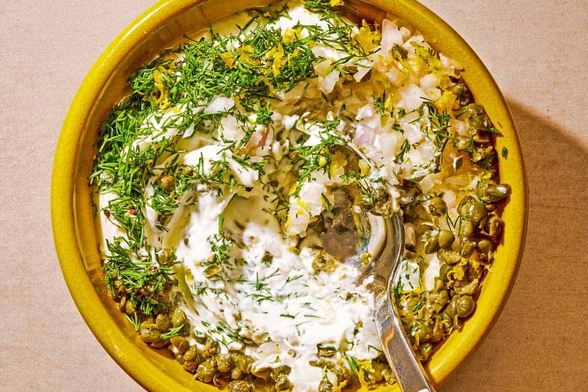 The yogurt-dill sauce for the salmon sandwich in a bowl with a spoon.