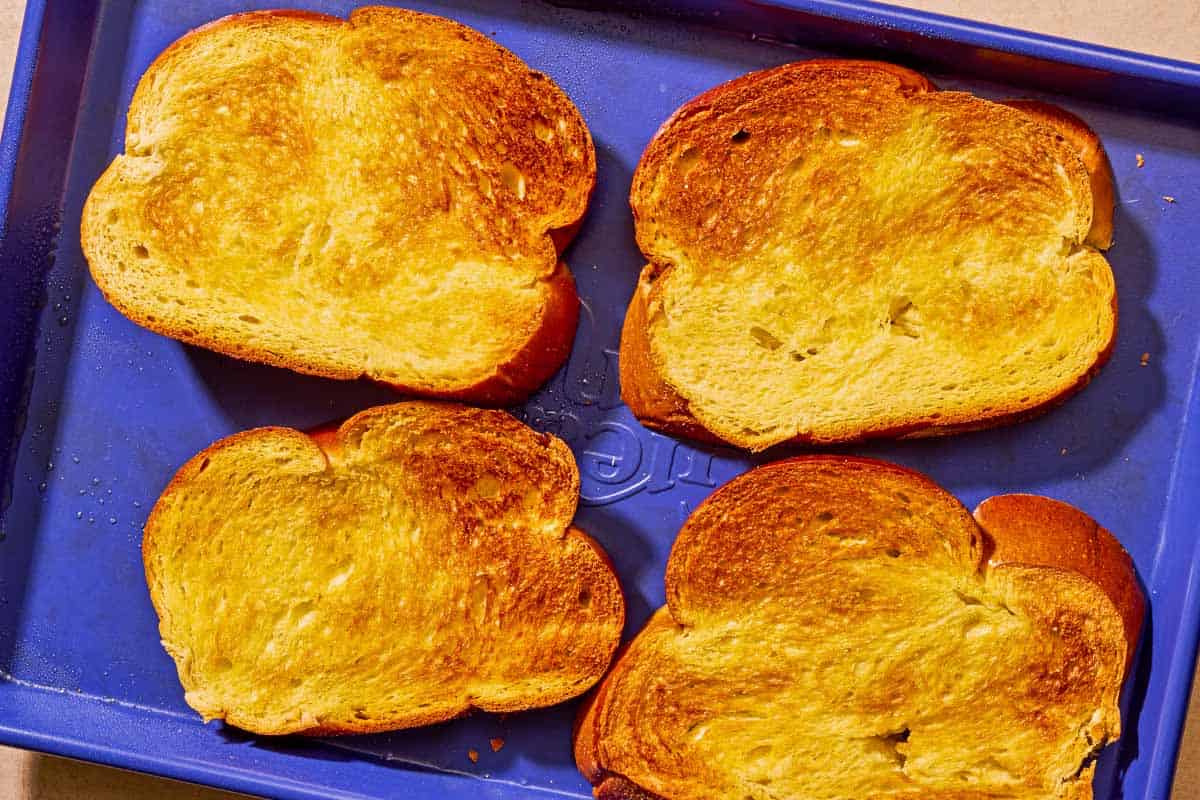 Four slices of toasted challah bread on a sheet pan.