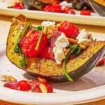 A close up of a stuffed acorn squash half on a plate in front of the rest of the stuffed acorn squash halves on a platter.