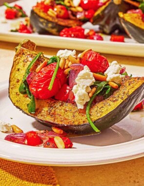 A close up of a stuffed acorn squash half on a plate in front of the rest of the stuffed acorn squash halves on a platter.