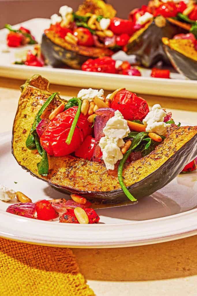 A close up of a stuffed acorn squash half on a plate in front of the rest of the stuffed acorn squash halves on a platter.