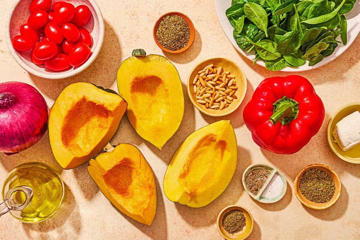 Ingredients for stuffed acorn squash including 4 acorn squash halves, olive oil, red onion, cherry tomatoes, spinach, red bell pepper, goat cheese, pine nuts, salt, black pepper, dried oregano, dried basil and dried thyme.