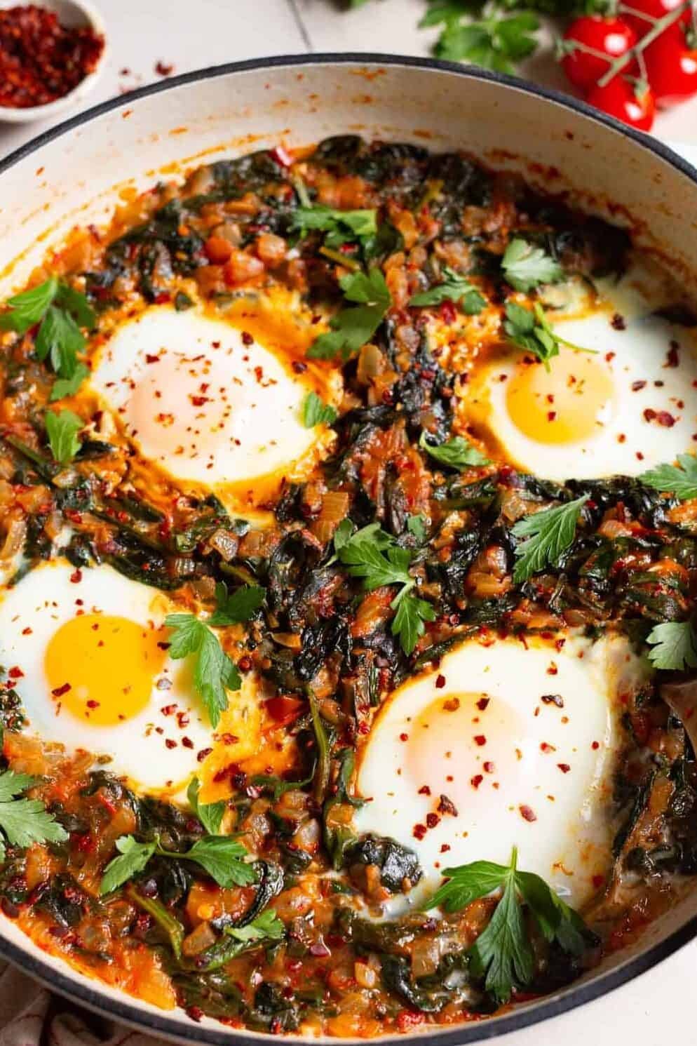 Side shot of a pan with Turkish spinach and eggs, showing the 4 poached eggs and saucy wilted spinach mixture.