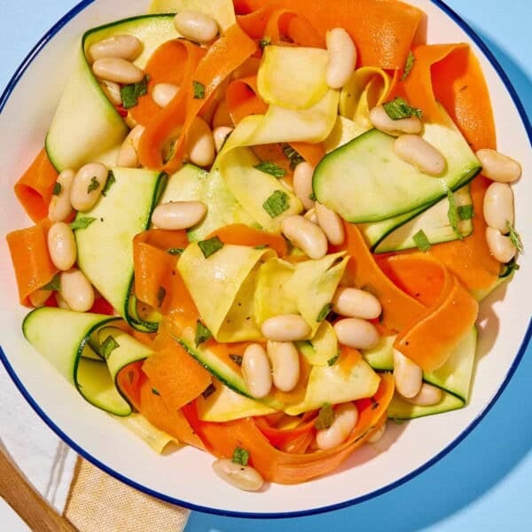 Zucchini ribbon salad in a bowl next to a cloth napkin, and a wooden spoon.