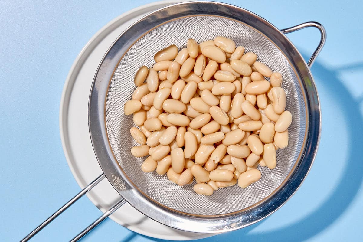 Cannellini beans in a strainer over a bowl.